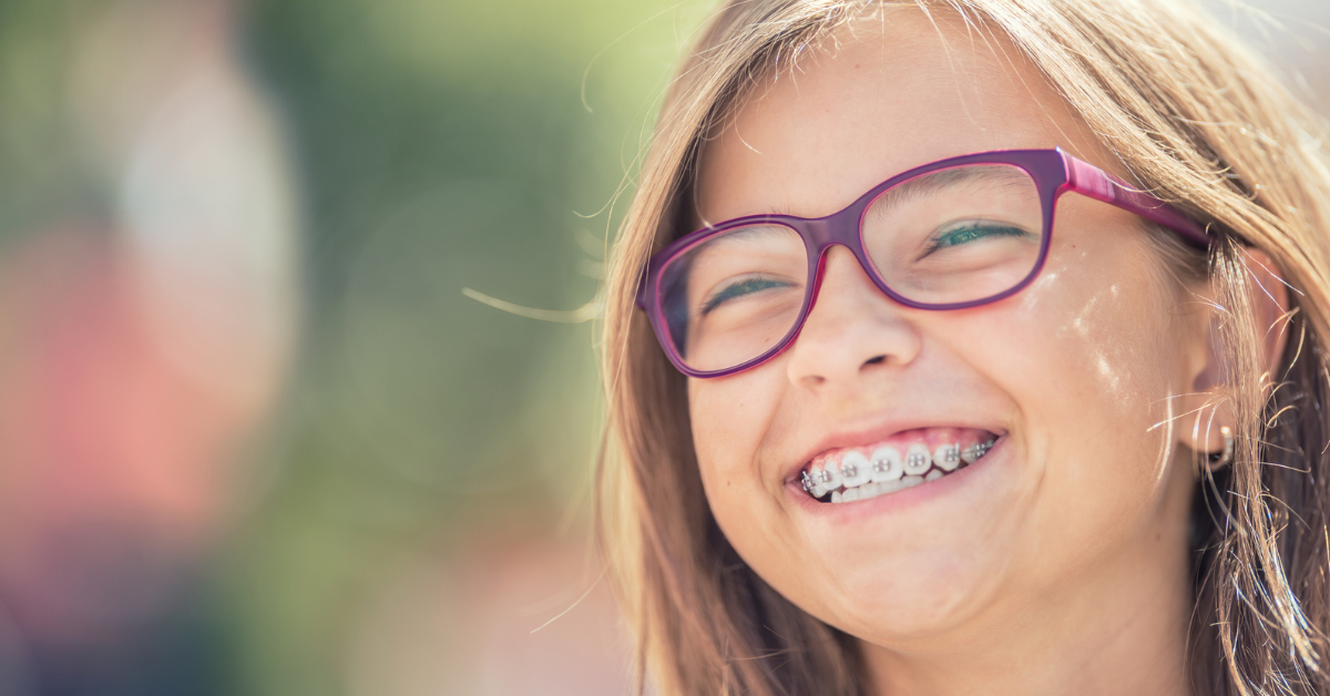 A young girl with glasses and braces smiles brightly, showcasing her joyful expression and enthusiasm.